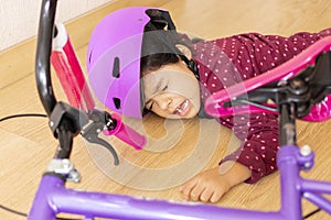 Sad little girl fell to the ground while playing with her bicycle in the floor