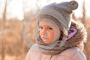 Sad little girl in a hat and a scarf on a walk in the autumn park