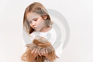 sad little girl holds in hands cropped hair after cutting on a white background