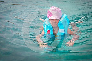A sad little girl in a life jacket tries to swim in the ocean. Portrait of a frightened child in the sea. A baby is saved after a