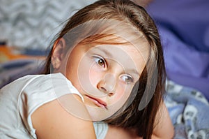 Sad little girl lying in bed in the bedclothes
