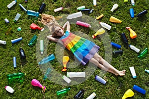 Sad little girl lying on the garbage filled grass