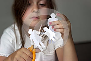 Sad little girl with paper family and scissors; divorce or family problems concept