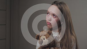 Sad little girl praying while holding a teddy bear in her hands. The teenager seeks protection from God. A lonely child