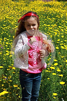 Sad little girl with a red bow in her hair. Girl with a dol on a green meadow among yellow flowers