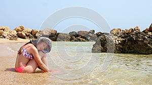 Sad little girl sit lonely on a sandy beach, enjoying warm water of the sea. summer holidays at the seaside
