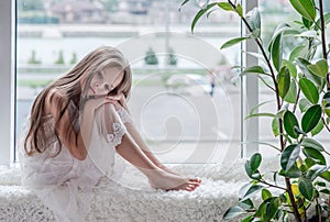 Sad little girl sits alone front of the window