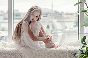 Sad little girl sits alone front of the window