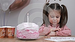 Sad little girl sits at a festive table next to a birthday cake.