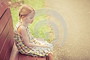 Sad little girl sitting on bench in the park