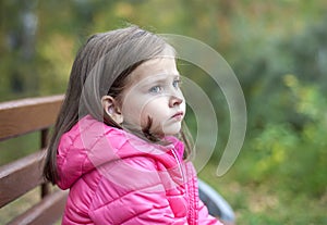 Sad little girl sitting on bench in the park at the day