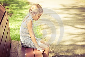 Sad little girl sitting on bench in the park