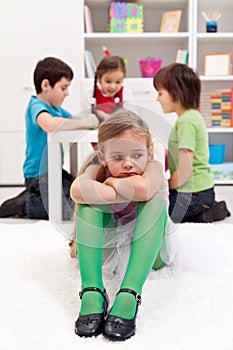Sad little girl sitting excluded by friends photo