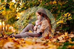 Sad little girl sitting on ground in fallen leaves. children`s resentment