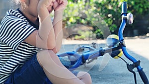 Sad little girl sitting on the ground after falling off her bike at summer park. Child was injured while riding a bicycle.