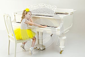 Sad little girl sitting leaning on a white Grand piano.