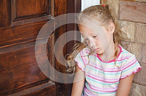 Sad little girl sitting near a door