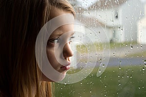 Sad little girl staring out rainy window