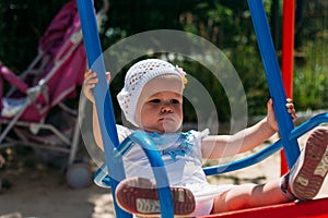 Sad, little girl in a white dress and hat, riding on a swing, summer sun and heat. playground. childhood, serenity. negative