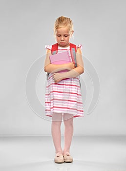 Sad little student girl with school bag and book