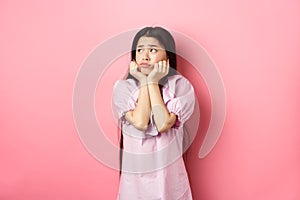 Sad and lonely asian girl look left and frowning, standing distressed against pink background