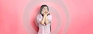 Sad and lonely asian girl look left and frowning, standing distressed against pink background