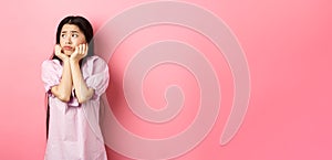 Sad and lonely asian girl look left and frowning, standing distressed against pink background