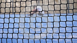 Sad lonely boy covered his face with hands sitting on the ground outdoors. View through the tennis net