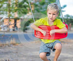 Sad lonely boy sitting on swing, waiting for friends or while parents are busy. Summer, childhood, leisure, friendship