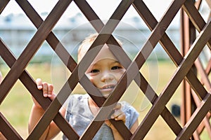 Sad and lonely child looking out through fence. Social problems, family abuse, children stress negative emotions