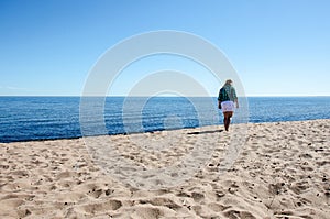 Sad lonely female walks solo on the beach on a sunny summer day