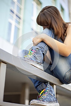 Sad lonely girl meditates sitting on the railing of city (focus