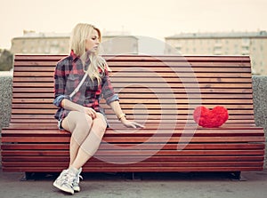 Sad lonely girl sitting on a bench near to a big red heart