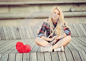 Sad lonely girl sitting on wood planks near to a big red heart