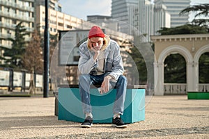 Sad lonely hipster guy sitting on bench feeling frustrated after reading sms on smartphone