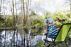 Sad and lonely kid boy with a fishing rod sits on the shore of the lake