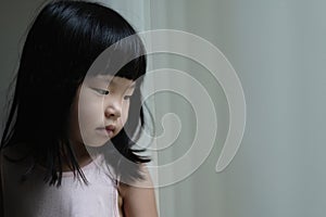 Sad lonely little girl standing beside a window