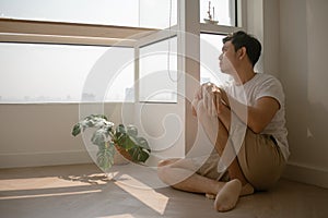 Sad and lonely man sits on the floor hugging his knee.