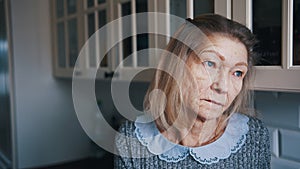 Sad lonely old gray haired woman looking through the window. Vulnerable person in quarantine