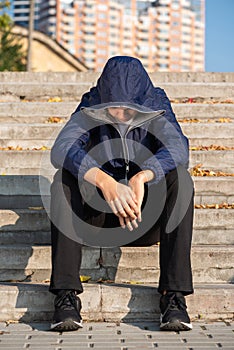 Sad lonely troubled teenage boy with hands down sitting on steps outdoors