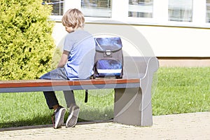 Sad, lonely, unhappy, disappointed boy sitting alone near school. Backpack. Casual clothes. Outdoor