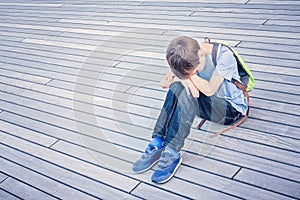 Sad, lonely, unhappy, disappointed child sitting alone on the ground outdoors