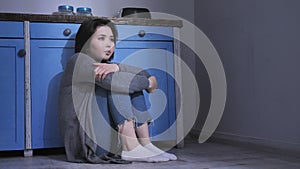 Sad lonely young Asian girl sitting on the floor in kitchen, holding her knees with arms, domestic violence concept 50