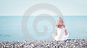 Sad lonely young beautiful woman sitting back on beach the sea