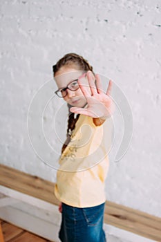 Sad long hair tweens girl in glasses pulling hand towards camera on white wall background photo