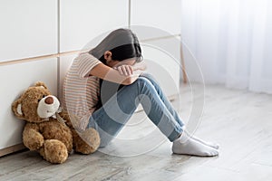 Sad long-haired little girl sitting by wall with toy