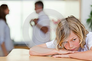 Sad looking boy with fighting parents behind him