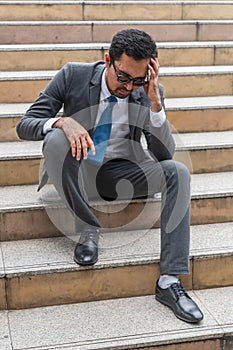 A sad looking young businessman sitting at the staircase