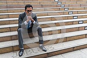 A sad looking young businessman sitting at the staircase