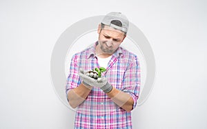 Sad male gardener holds and looking getting rotten plant, isolated on white background. Sorrowful male farmer feeling miserable